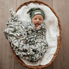 Sleeping baby wrapped in Snuggle Hunny Kids Evergreen Organic Muslin Wrap laying in a basket